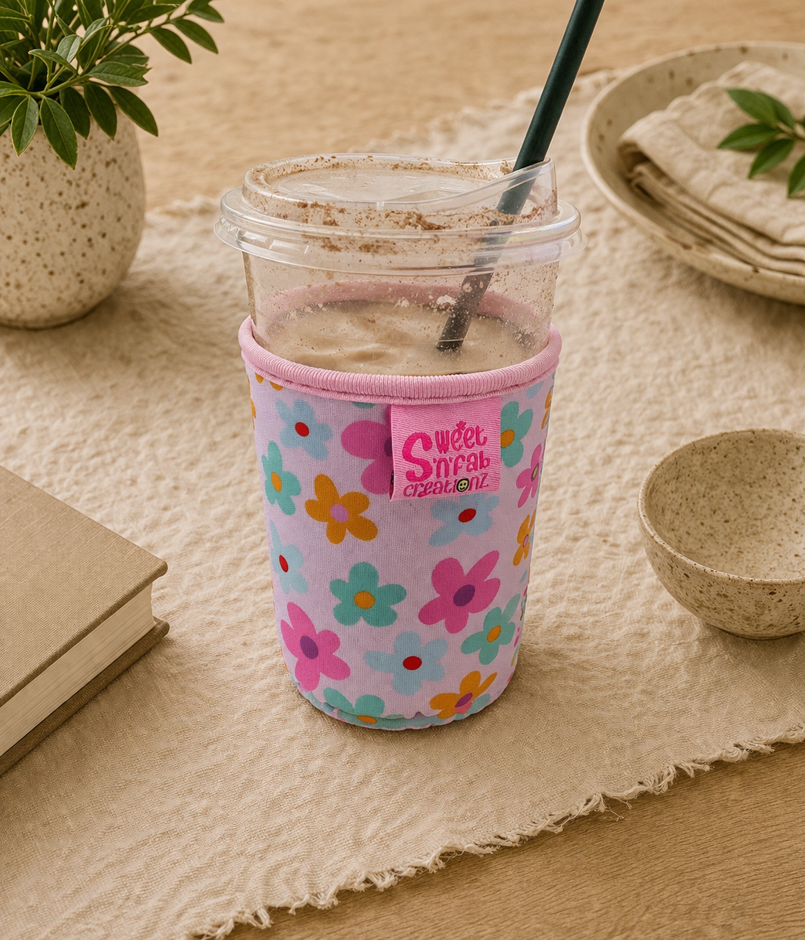 Cup with floral sleeve on a table with a plant and bowls in the background